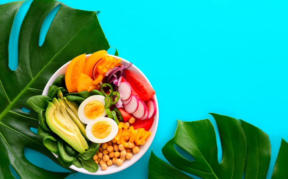 Freshly cooked Buddha bowl salad served on summer style decorated table, view from above, blank space for a text