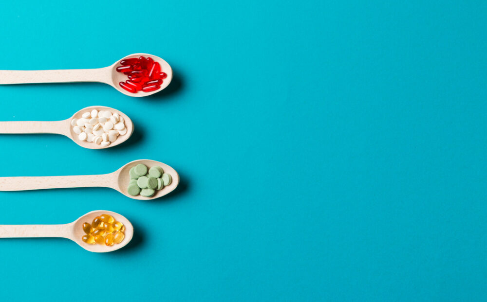 Top view Variety of vitamin and mineral pills in wooden spoon on Colored background. Top view of assorted pharmaceutical medicine pills. Dietary supplement healthcare product.