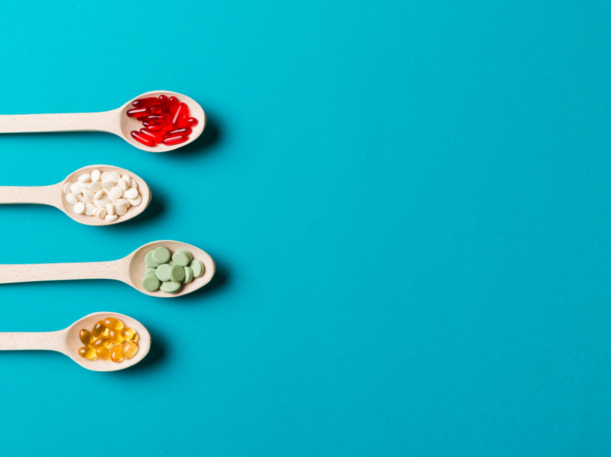 Top view Variety of vitamin and mineral pills in wooden spoon on Colored background. Top view of assorted pharmaceutical medicine pills. Dietary supplement healthcare product.